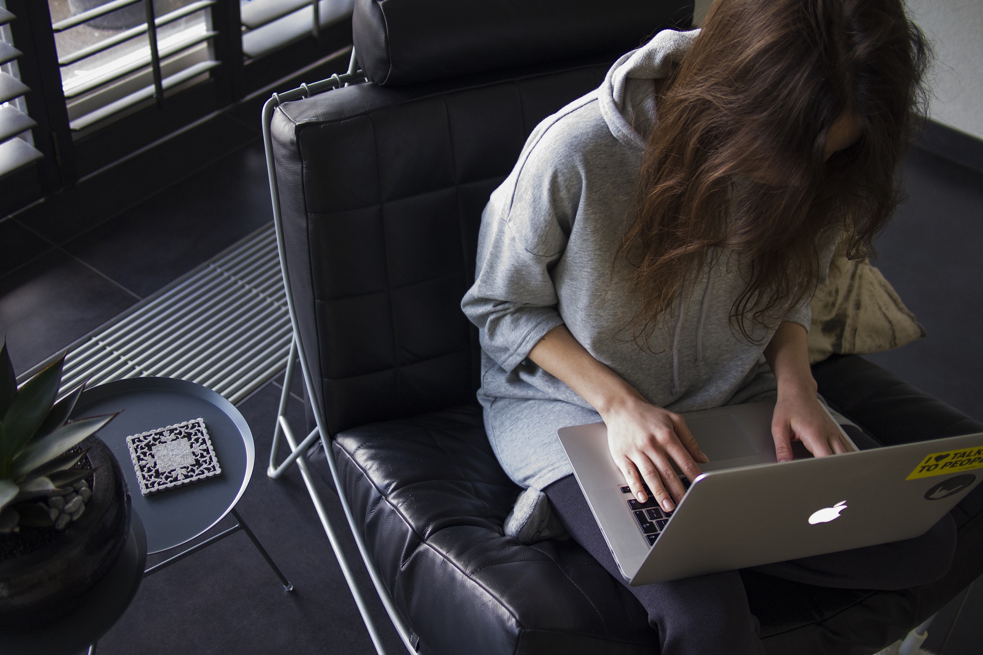 uma mulher, sentada em uma poltrona com um macbook no colo, suas mãos sobre as teclas